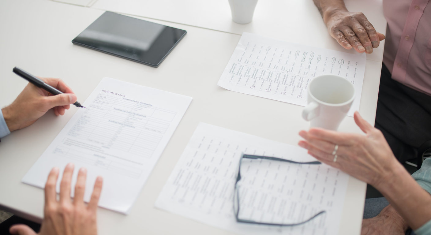 Hands reviewing printed forms around a table.